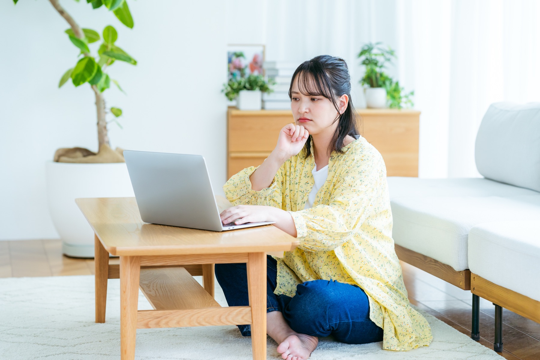ローテーブルでノートPCを操作しながら考える女性