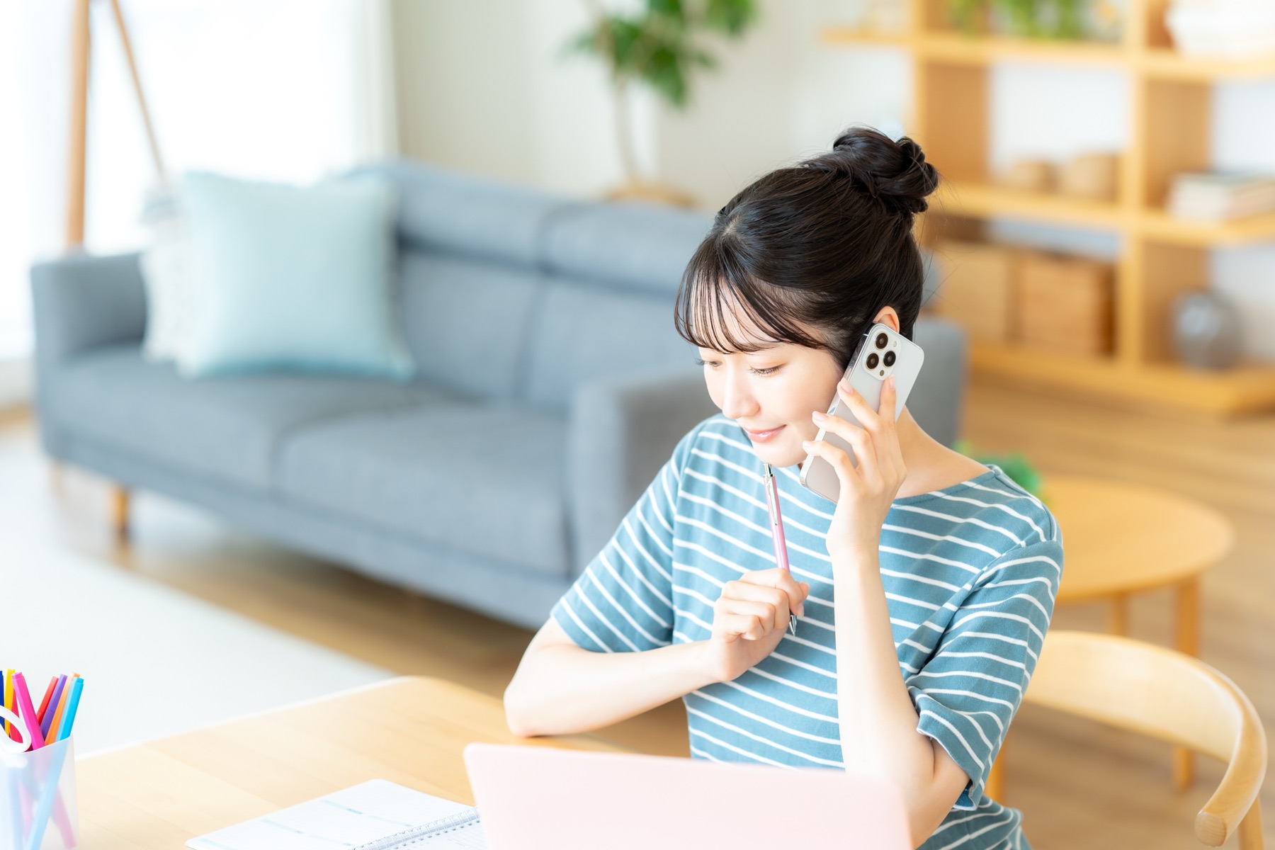 ノートPCの前でスマホで通話する女性