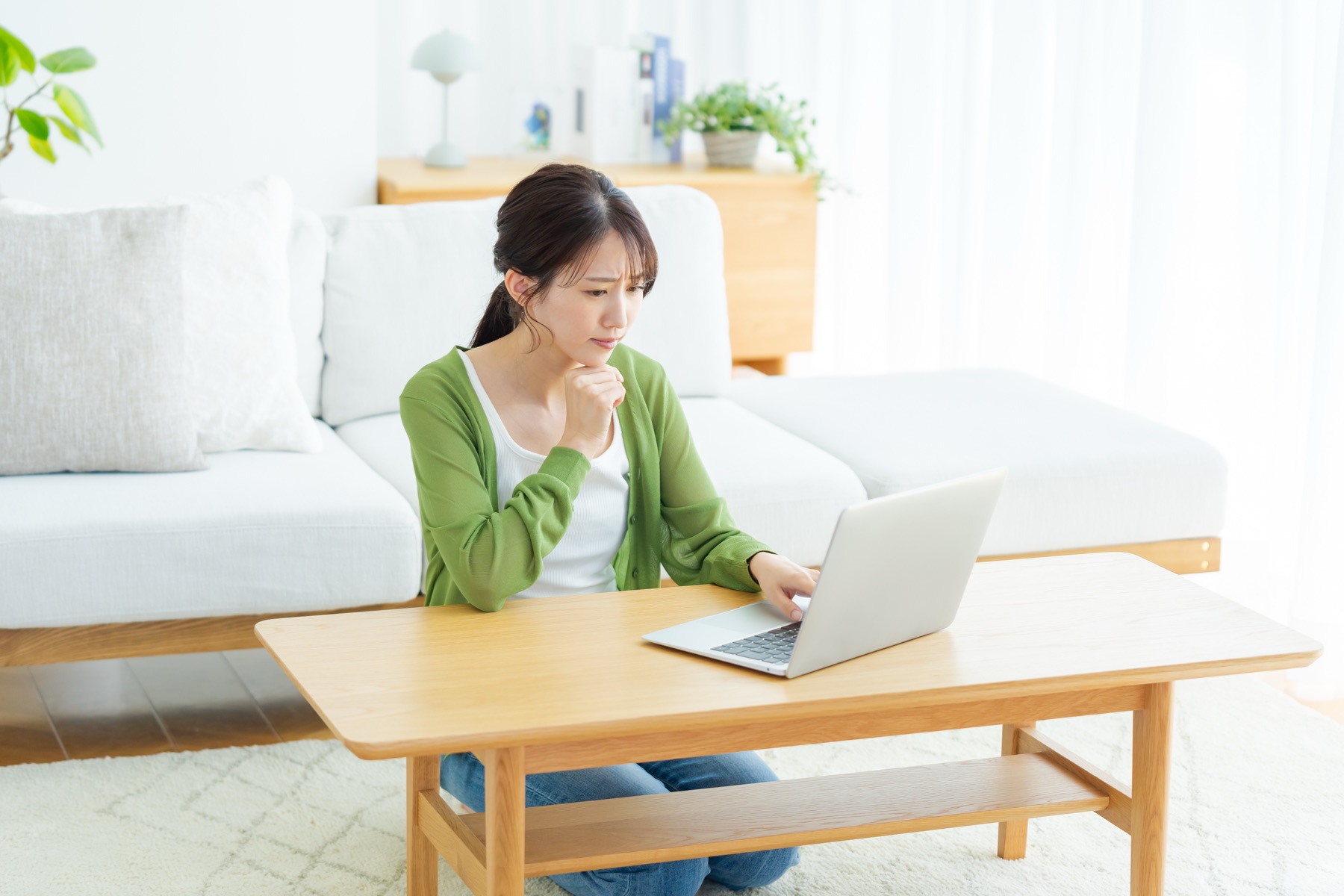 自宅ソファ前でノートPCを見ながら考え込む女性